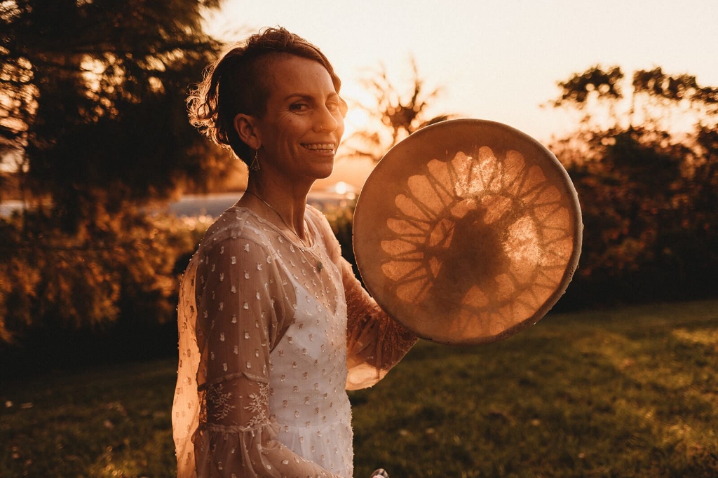 Sound healing practitioner holding a frame drum during a sunset sound bath session by LionHeartCircle