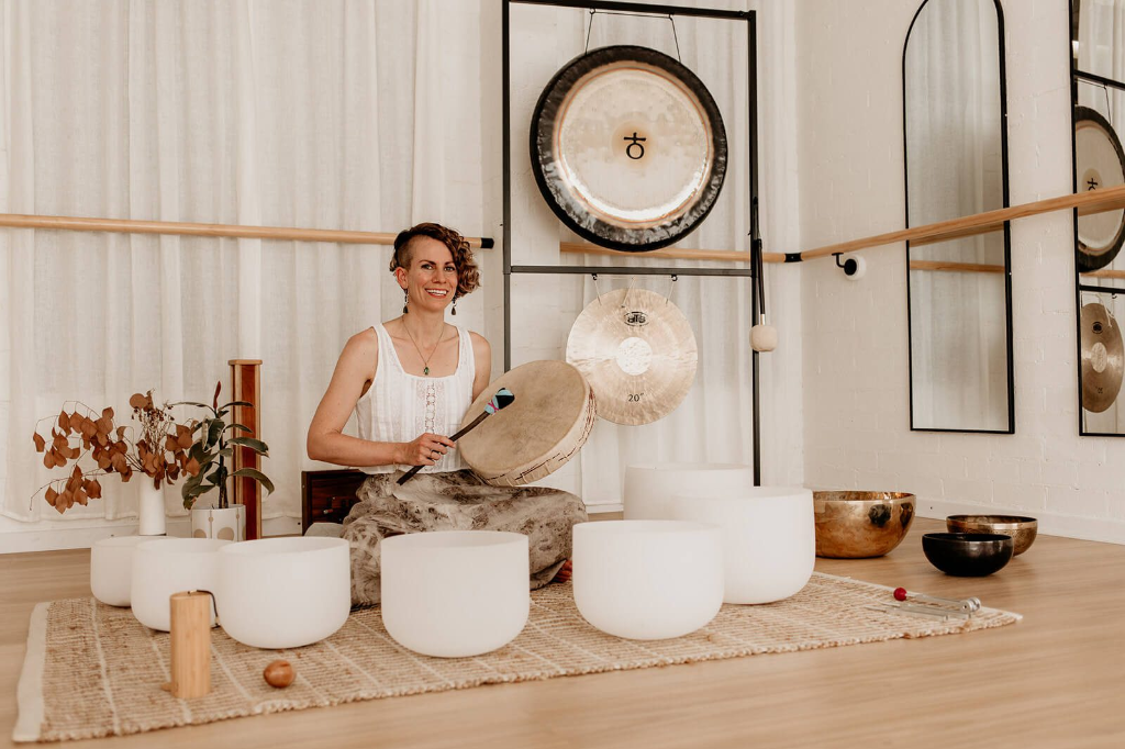Sound healing practitioner surrounded by crystal singing bowls and gongs in a calming studio environment by LionHeartCircle